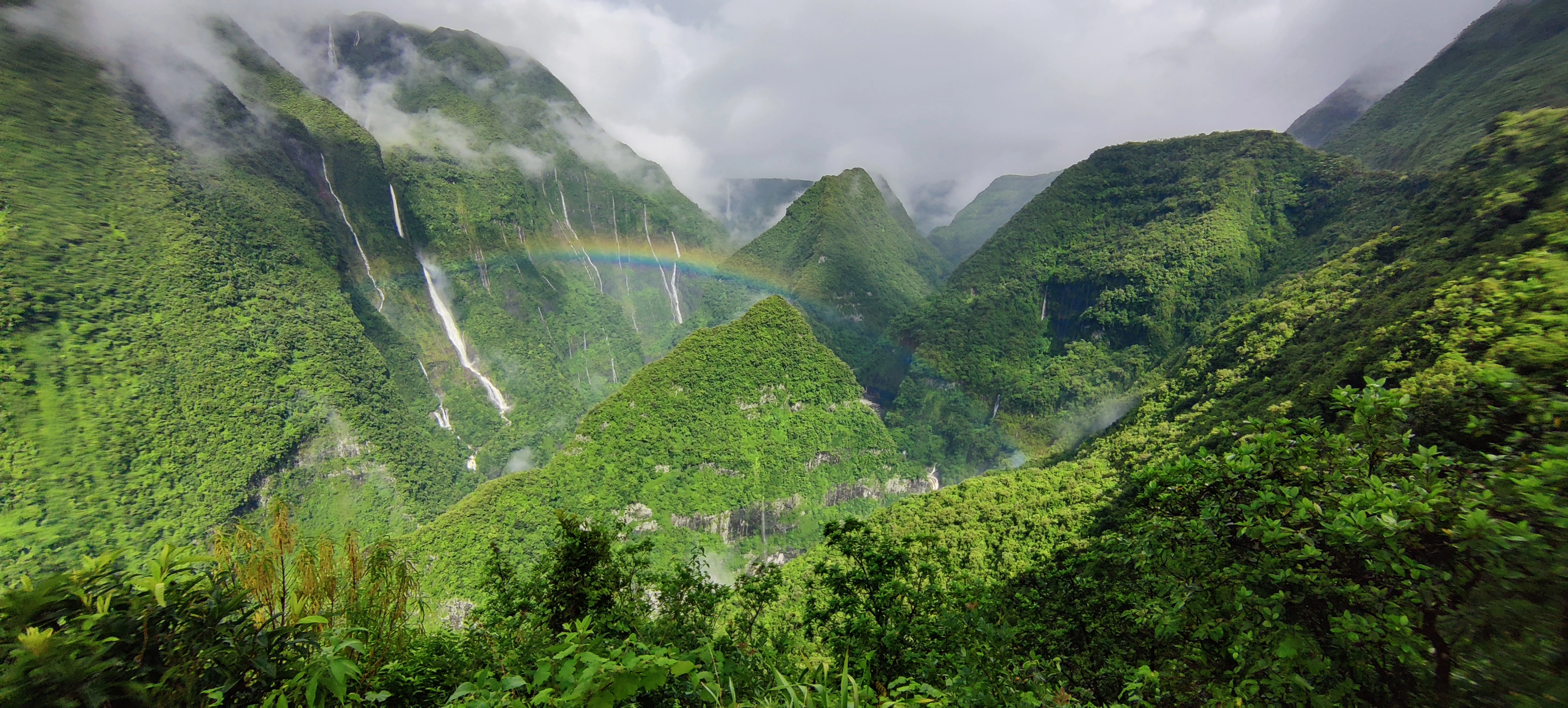 Photo d'un panorama Réunionnais : un arc en ciel au milieu de falaises et d'un océan de verdure